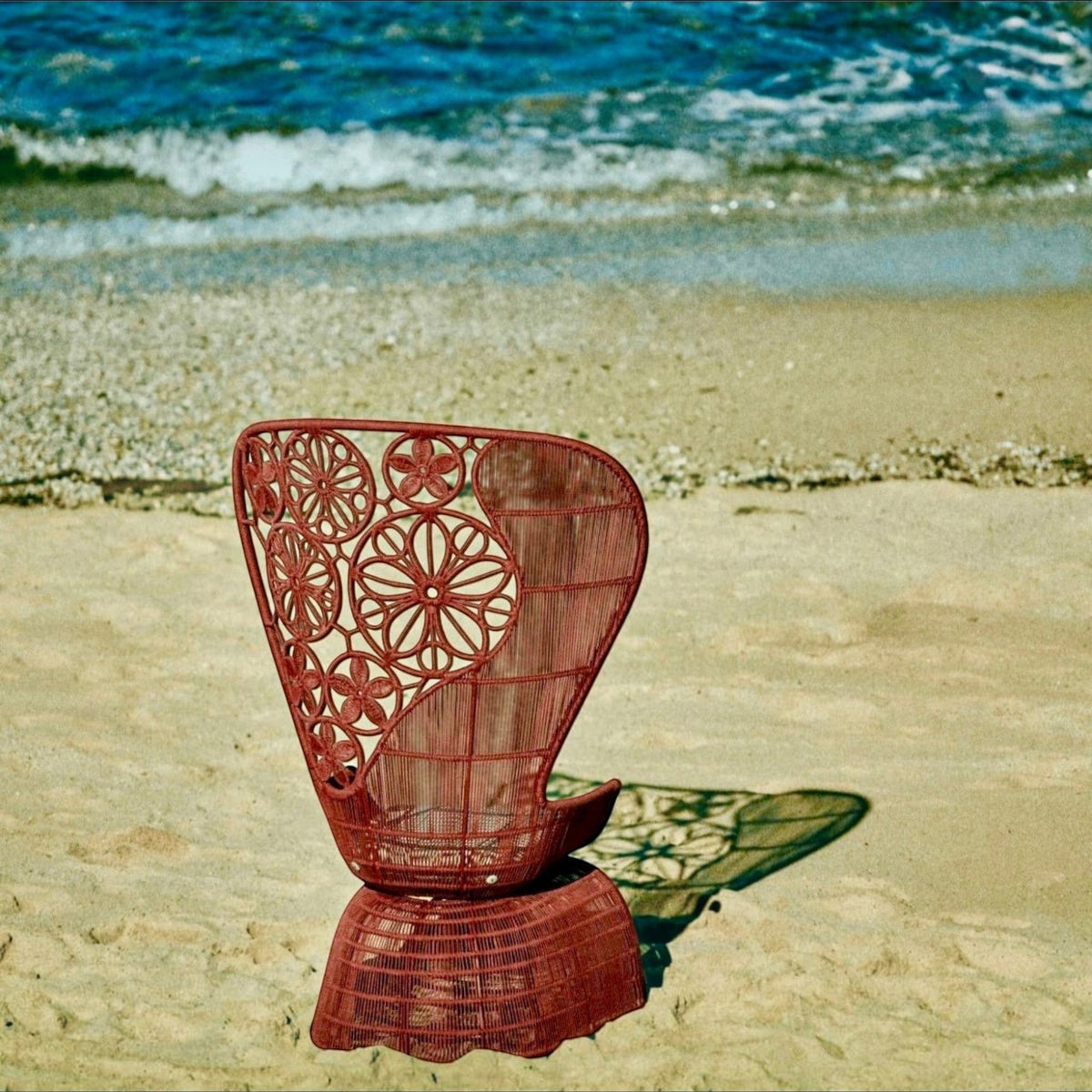 Urban Ashram Genevieve high-back armchair with intricate floral woven backrest on a sandy beach by the ocean.