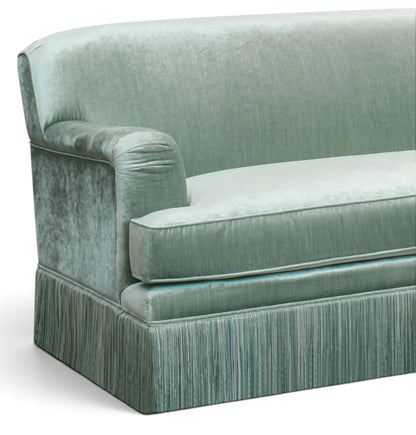 Urban Ashram vintage-style green velvet sofa with elegant tassel fringe and rounded armrest detail.