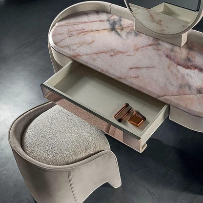 Urban Ashram Aveline vanity with pink veined marble top, open drawer, and matching upholstered stool in a curved design.