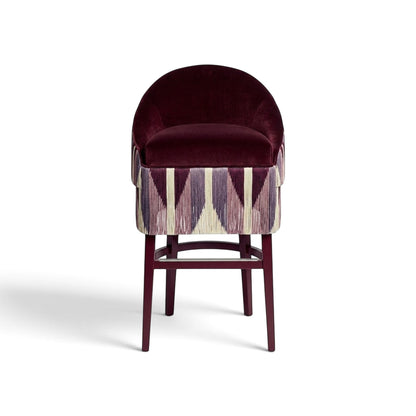 Urban Ashram Atelier fringe bar stool with a plum velvet seat and geometric patterned fringe skirt on wooden legs.