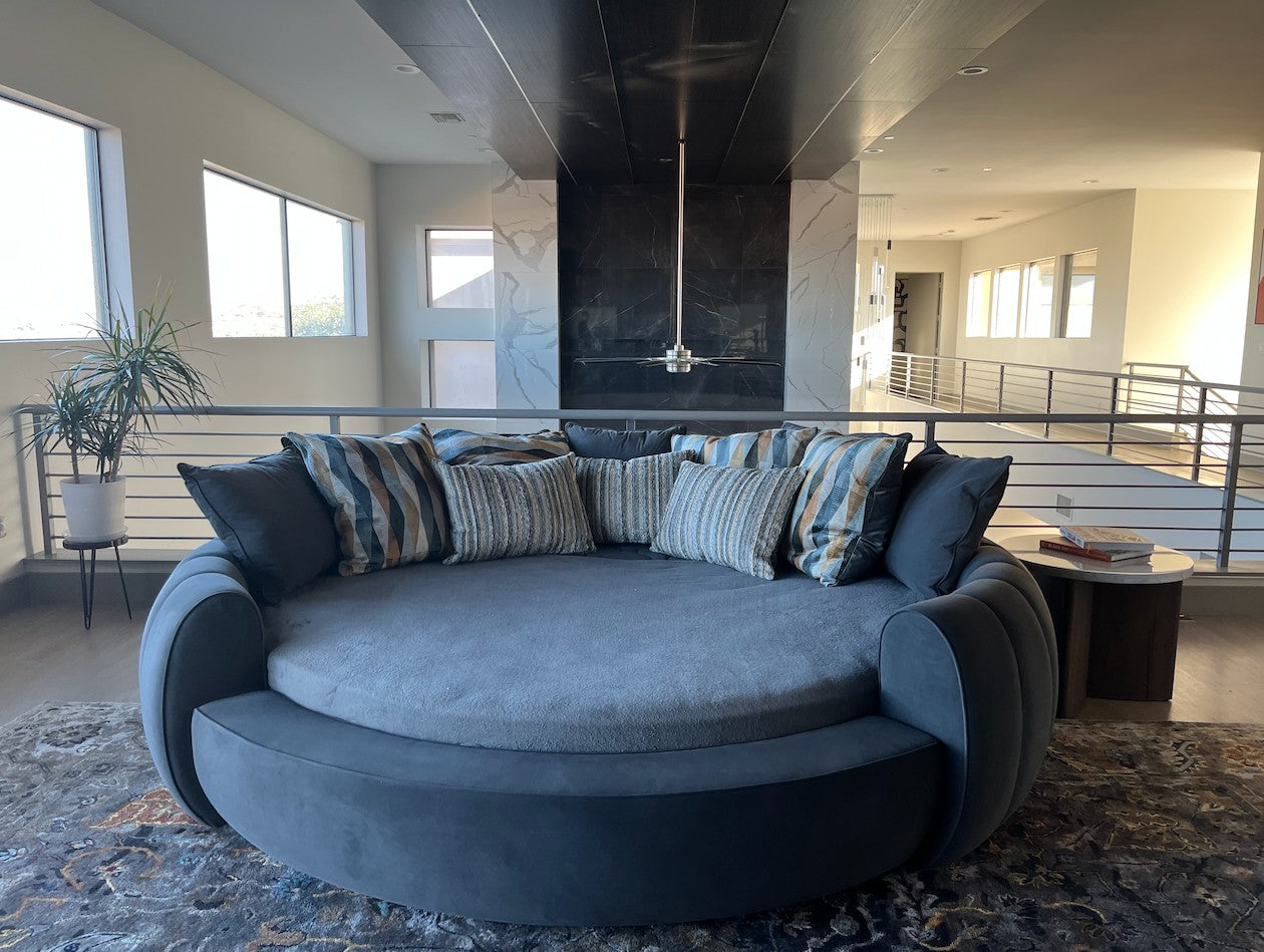 Urban Ashram Dream Lounger round movie bed in dark grey velvet with plush striped accent pillows in a modern living room